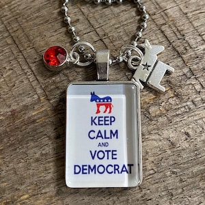 May include: A silver charm necklace with a red rhinestone, a silver donkey charm, and a square glass charm with a blue and red donkey and the text "Keep Calm and Vote Democrat".