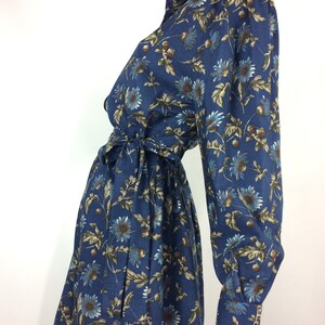 Puede incluir: Un vestido azul de manga larga con estampado floral. El vestido tiene cuello, cierre de botones en la parte delantera y un cintur&oacute;n de lazo en la cintura.