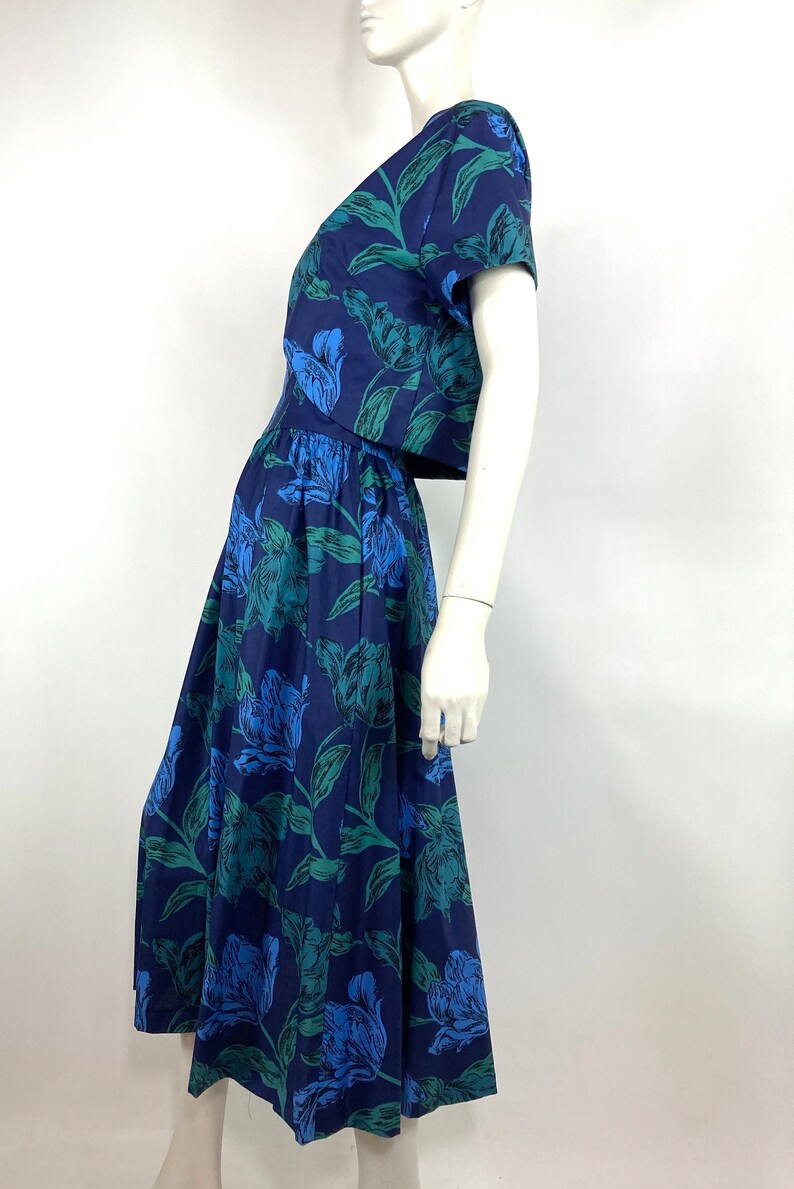 K&ouml;nnte beinhalten: Ein zweiteiliges Kleid mit blauem und gr&uuml;nem Blumendruck, bestehend aus einem Crop-Top und einem Midirock.