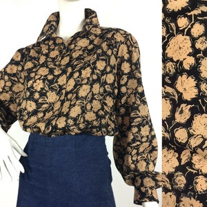 May include: A black and brown floral print blouse with long sleeves and a button-up front. The blouse has a relaxed fit and a slightly gathered detail at the cuffs.