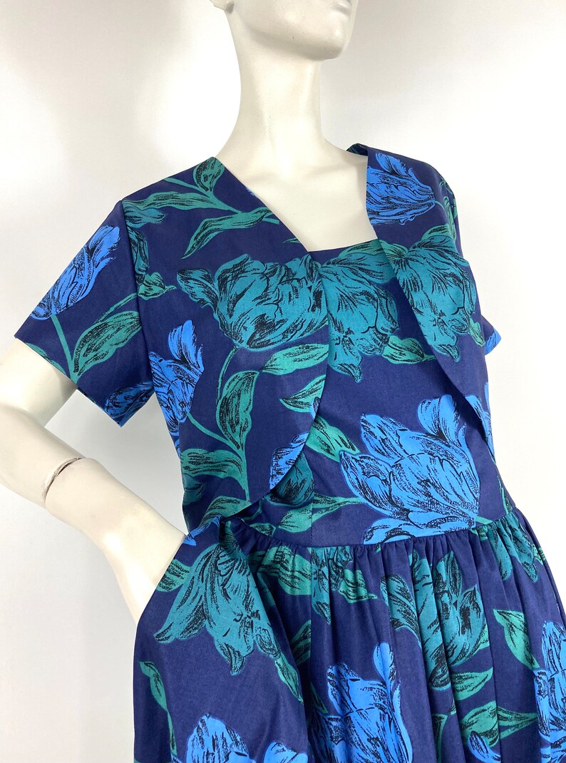 K&ouml;nnte beinhalten: Ein marineblaues Kleid mit einem Blumendruck aus blauen und gr&uuml;nen Tulpen. Das Kleid hat einen V-Ausschnitt und kurze &Auml;rmel. Der Rock ist in der Taille gerafft.
