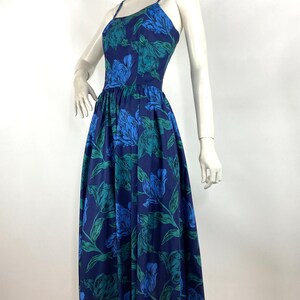 K&ouml;nnte beinhalten: Ein blaues Midikleid mit einem Blumendruck mit gr&uuml;nen Bl&auml;ttern und blauen Bl&uuml;ten. Das Kleid hat einen taillierten Oberteil und einen weiten Rock.