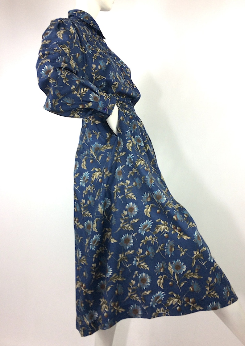Puede incluir: Un vestido de estampado floral azul y marr&oacute;n con falda larga y mangas largas. El vestido tiene cuello y cierre de botones en la parte delantera.