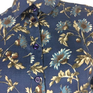 Puede incluir: Una camisa azul marino de botones con estampado floral con flores marrones, azules y blancas. La camisa tiene un cuello cl&aacute;sico y cierre de botones.