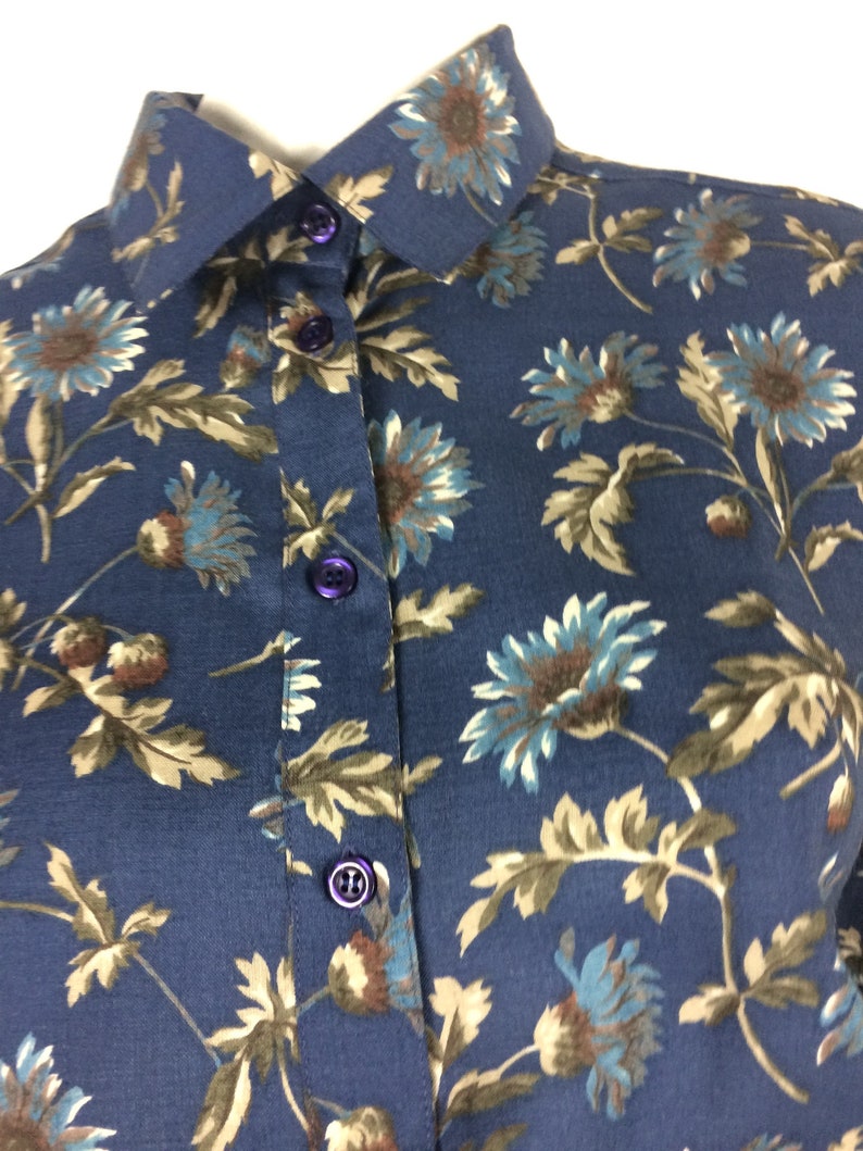 Puede incluir: Una camisa azul marino de botones con estampado floral con flores marrones, azules y blancas. La camisa tiene un cuello cl&aacute;sico y cierre de botones.