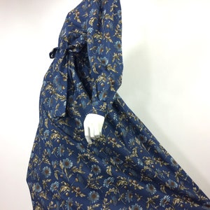 Puede incluir: Un vestido azul de manga larga con estampado floral. El vestido tiene un lazo en la cintura y una falda ligeramente acampanada.