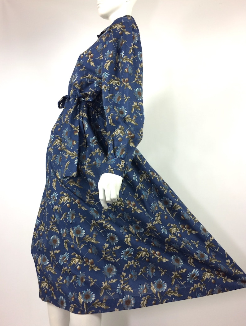 Puede incluir: Un vestido azul de manga larga con estampado floral. El vestido tiene un lazo en la cintura y una falda ligeramente acampanada.
