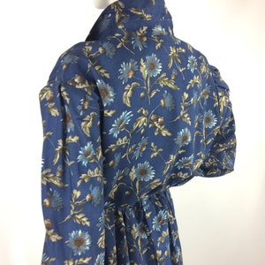 Puede incluir: Un vestido azul de manga larga con estampado floral. El vestido tiene una cintura fruncida y un cuello.