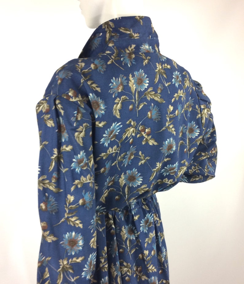 Puede incluir: Un vestido azul de manga larga con estampado floral. El vestido tiene una cintura fruncida y un cuello.