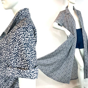 Puede incluir: Un vestido largo de estampado floral azul marino y blanco con cuello y mangas cortas. El vestido tiene una abertura frontal y una falda fluida.