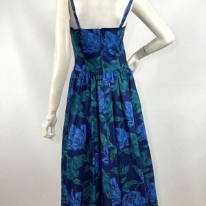 K&ouml;nnte beinhalten: Ein blaues und gr&uuml;nes Blumenmuster-Midi-Kleid mit d&uuml;nnen Tr&auml;gern. Das Kleid hat ein tailliertes Oberteil und einen vollen Rock.