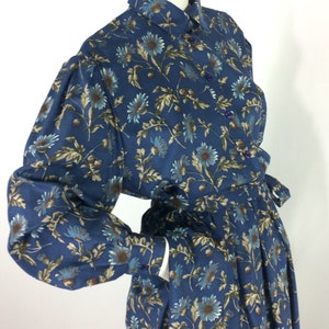 Puede incluir: Un vestido azul de manga larga con estampado floral. El vestido tiene cuello, cierre de botones y cintur&oacute;n de lazo. El vestido est&aacute; hecho de una tela ligera y tiene un corte holgado.