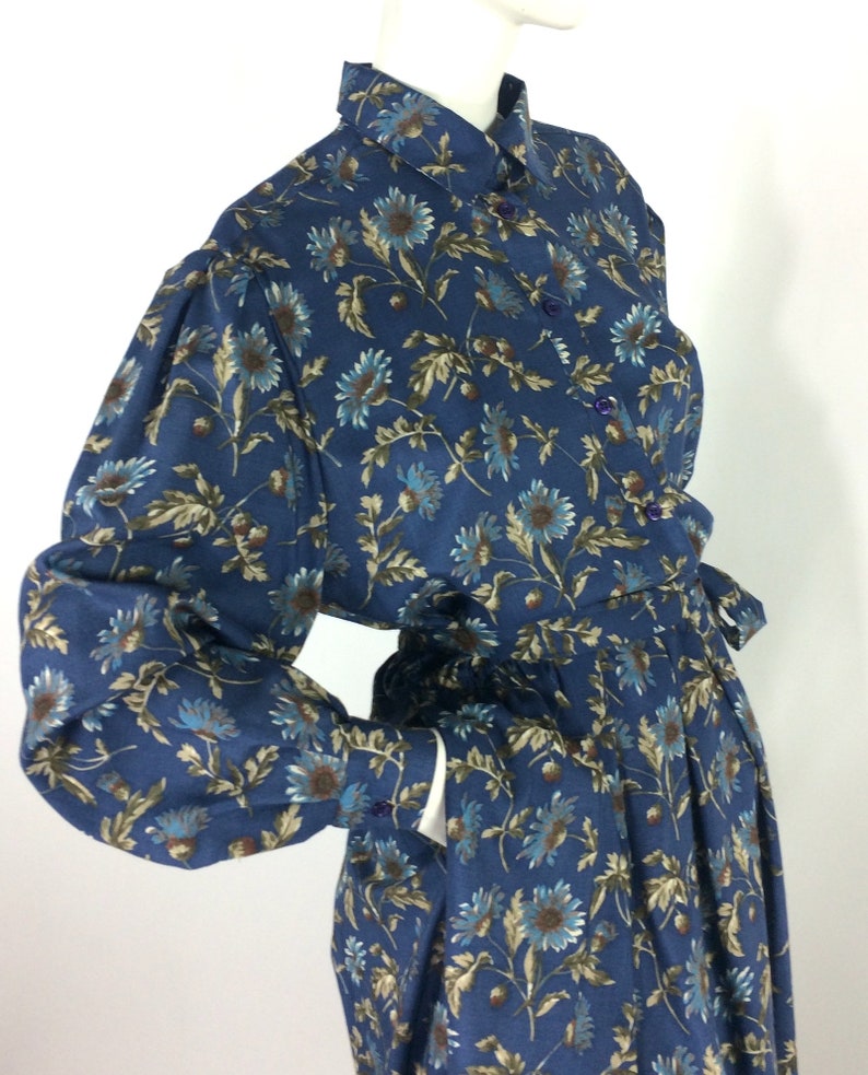 Puede incluir: Un vestido azul de manga larga con estampado floral. El vestido tiene cuello, cierre de botones y cintur&oacute;n de lazo. El vestido est&aacute; hecho de una tela ligera y tiene un corte holgado.