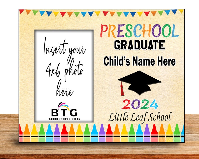 May include: A wooden photo frame with a cream-colored background. The frame has a space for a 4x6 photo and is decorated with colorful crayons and pennants. Text includes "Preschool Graduate," "Child's Name Here," and "2024 Little Leaf School."