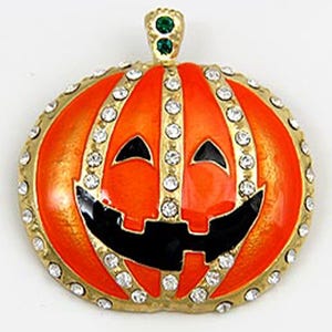 May include: A round, orange pumpkin brooch with a smiling jack-o'-lantern face. The brooch has a gold-colored border and is embellished with clear rhinestones. Two green stones are set at the top.
