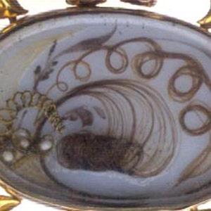 May include: A gold locket with a glass front containing a hair wreath. The hair is arranged in a spiral pattern with a small cluster of pearls at the bottom.