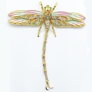 May include: A gold-toned dragonfly brooch with colorful rhinestones and enamel wings in shades of pink, green, and gold. The brooch features intricate detailing and a delicate design, perfect for adding a touch of elegance to any outfit.