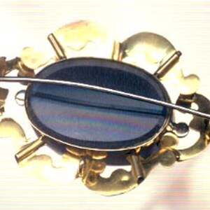 May include: A gold-toned brooch with a black oval cameo set in a floral design.