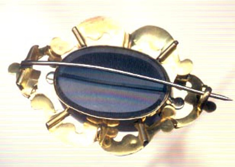 May include: A gold-toned brooch with a black oval cameo set in a floral design.