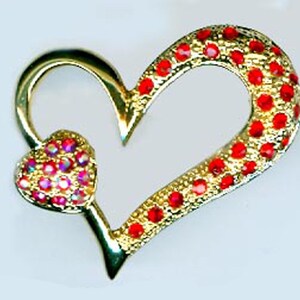May include: A gold heart-shaped pendant with red rhinestone accents. The pendant has a small heart-shaped design in the center, also adorned with red rhinestones.