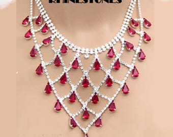 May include: A sparkling silver necklace with a diamond-patterned design, adorned with numerous teardrop-shaped, ruby-red rhinestones. The necklace features the text "SWAROVSKI RHINESTONES" at the top.