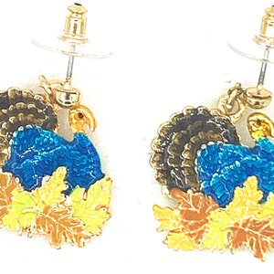 May include: A pair of gold tone earrings featuring a blue and brown turkey with gold accents and yellow, orange, and brown leaves.
