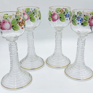 May include: Four clear glass wine glasses with gold rims and hand-painted floral designs in pink, blue, and green.