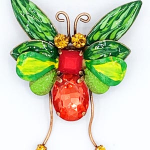 May include: A green and yellow butterfly brooch with red and orange rhinestones. The butterfly has a wire body and antennae.