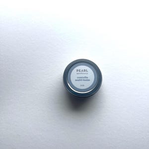 May include: A small, round, dark blue container of Pearl Apothecary centella multi-balm. The label is white with black text, and the container is 3 oz.