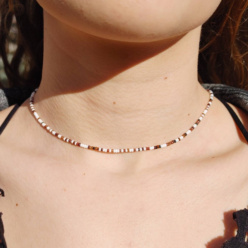 May include: A delicate choker necklace made with small white and brown beads. The necklace is simple and elegant, perfect for everyday wear.