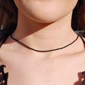 May include: A simple black beaded choker necklace. The necklace is made of small, black beads and is worn by a person.