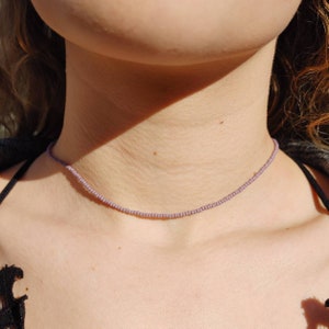May include: A delicate choker necklace made with small, light purple beads. The necklace is simple and elegant, perfect for everyday wear.