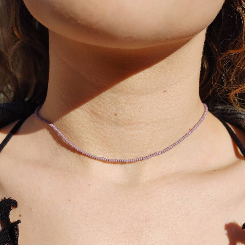 May include: A delicate choker necklace made with small, light purple beads. The necklace is simple and elegant, perfect for everyday wear.