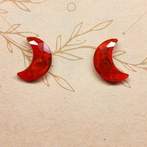 May include: A pair of red crescent moon earrings. The earrings are made of resin and have a marbled effect.