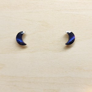 May include: A pair of crescent moon shaped earrings with a black and iridescent purple finish.
