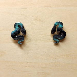 May include: A pair of black and green snake earrings with a glittery finish.