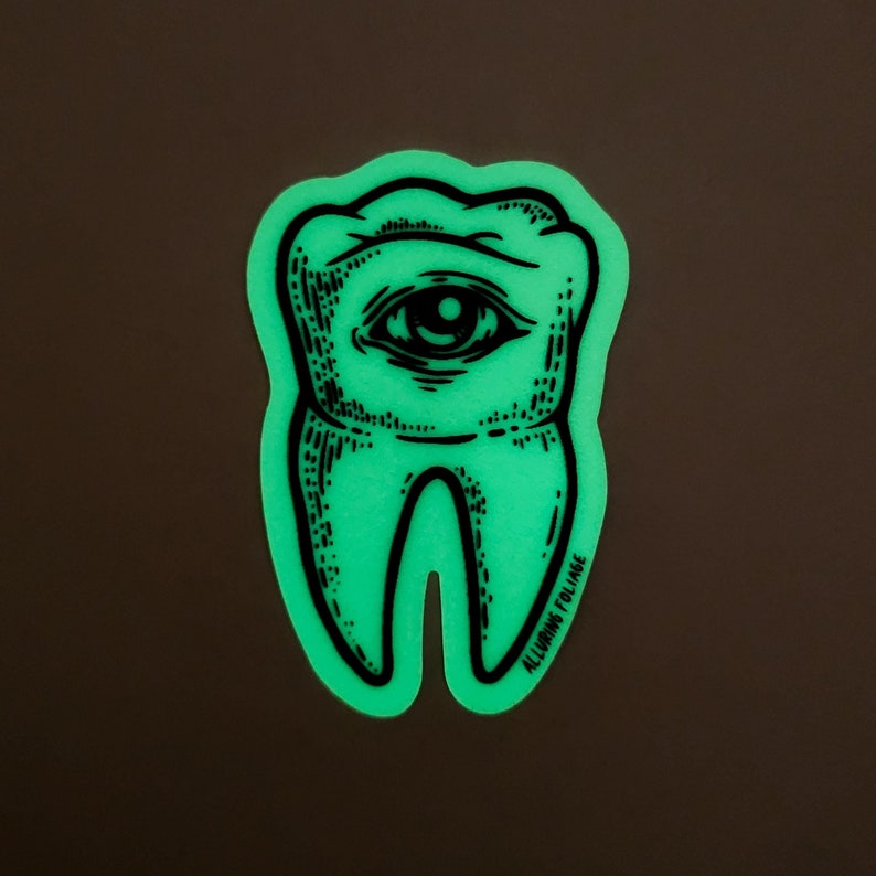 May include: A green glow-in-the-dark sticker of a tooth with an eye in the center. The sticker has the text "ALLUMIN FOLIAE" at the bottom.