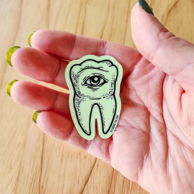 May include: A green glow-in-the-dark sticker of a tooth with an eye in the center. The sticker has the text "ALLIGATOR FOLIAE" at the bottom.