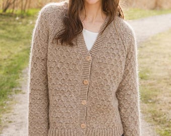 May include: A beige long-sleeve knit cardigan featuring a textured waffle-like pattern, a V-neckline, and a front button closure with four light-colored circular buttons. The garment has ribbed cuffs and a ribbed hem, worn over a white shirt.