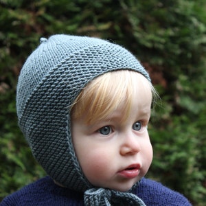 May include: A child wearing a blue knitted hat with ear flaps. The hat has a simple stitch pattern and is pulled down over the child's ears.