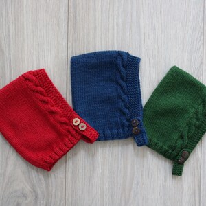 Puede incluir: Tres gorros tejidos en rojo, azul marino y verde bosque. Cada gorro presenta un patrón de punto trenzado texturizado a lo largo del borde frontal, un dobladillo inferior acanalado y dos pequeños botones circulares en una tira lateral.