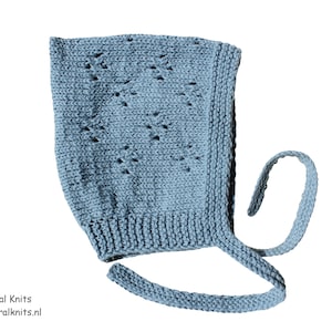 Op de afbeelding: Een lichtblauwe gebreide baby muts met een textuurontwerp en strikbandjes. De muts heeft een decoratief patroon aan de voorkant en een geribbelde rand. De tekst "Little Natural Knits" en een websiteadres zijn onderaan zichtbaar.