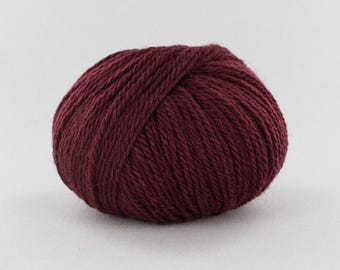 May include: A round ball of deep burgundy yarn featuring a tightly wound, multi-ply construction with a visible twisted texture. The yarn displays a consistent dark red color throughout, showcasing the individual strands of the fiber clearly.