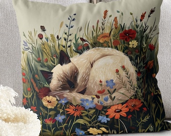 May include: A throw pillow with a white cat sleeping in a field of colorful flowers. The cat is curled up in a ball and has its eyes closed. The flowers are a variety of colors, including red, orange, yellow, blue, and purple.