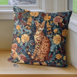 Könnte beinhalten: Ein dekoratives Kissen mit blauem Hintergrund, auf dem eine Bengal-Katze in einem Feld voller bunter Blumen sitzt. Die Katze ist braun und schwarz mit orangefarbenen Markierungen.