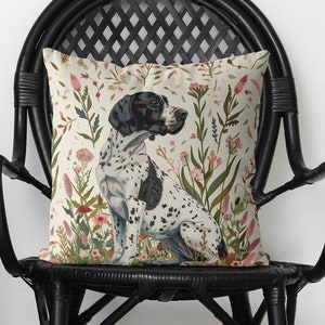 May include: A cream-colored throw pillow with a black and white dog illustration surrounded by colorful flowers. The pillow is sitting on a black wicker chair.