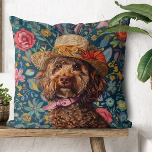 Op de afbeelding: Een bruine en witte hond die een strohoed draagt met bloemenaccenten en een roze strik. De hond zit op een blauw kussen met bloemenprint.