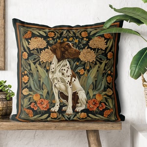 May include: A black and green throw pillow with a brown and white dog sitting in a garden of flowers. The dog is a pointer breed with brown and white spots. The flowers are red, yellow, and white.