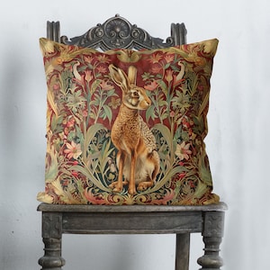 Peut inclure: Un coussin décoratif avec un motif floral rouge, vert et or mettant en scène un lièvre brun au centre.