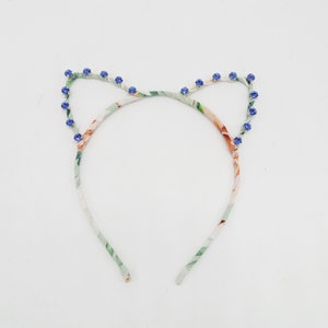 May include: A floral patterned headband with blue rhinestone accents in the shape of cat ears.